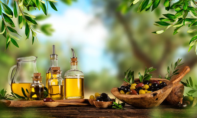 Freshly harvested olives berries in wood bowls and pressed oil in glass bottles