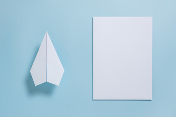 Flat lay of white paper plane and blank paper on pastel blue color background