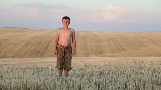 The boy is in the field, running, jumping, dancing and walking. A child is playing in a cleaned field.

