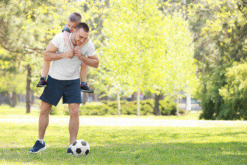 Father and son playing football on green grass in park