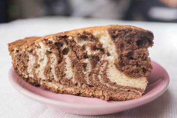 Piece of zebra pie on a saucer of mauve-colored on a white lace background, close-up