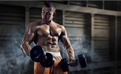 Fototapeta na wymiar Sport and fitness. Muscular bodybuilder in the gym training with dumbbells