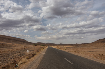 Road through Morocco steppe landscape with trees and mount at background. Area between Atlas mountains range and Sahara desert.