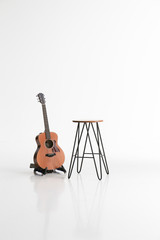 Acoustic guitar is on stand and chair on white background with soft shaodow and reflection on the floor