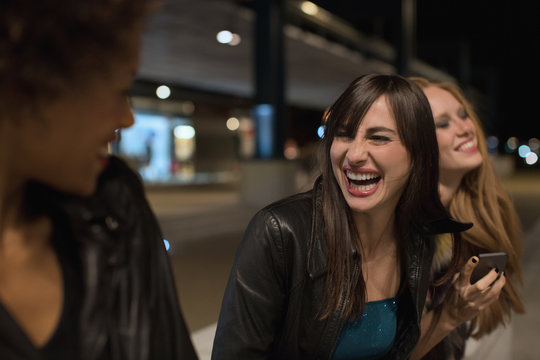 Three female friends sitting outside train station laughing before going out clubbing in the evening