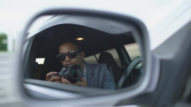 Reflection in side mirror of Paparazzi man sitting inside car and photographing with dslr camera