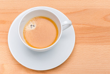 Hot black coffee with foam bubbles in white cup with wooden board in background, morning coffee concept.