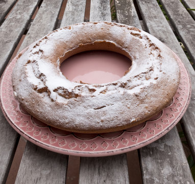 Ciambellone sprinkled with velvet sugar on ceramic plate decorated with pink confetti pad. All resting on wooden table.