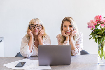 Grandmother with her granddaughter sitting at the table with laptop
