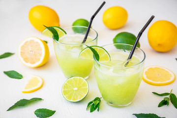 Fresh citrus lemonade with limes and lemons in glasses on white table