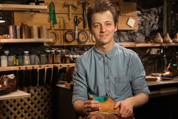 Cheerful shoemaker in workshop holding shoes