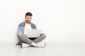 Young man working on laptop sitting on floor