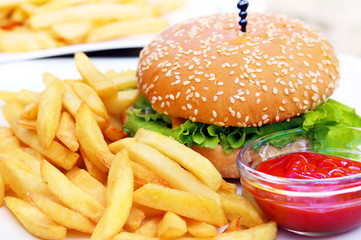 Burger with french fries and bowl of ketchup on white plate.