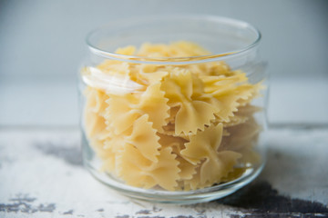 Pasta in the form of bows scattered from glass jar. Italian handmade pasta on the old background.