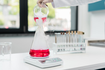 Cropped shot of scientist pouring reagent into flask on electronic scales in chemical laboratory