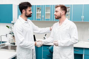 Obraz premium Professional young chemists in white coats shaking hands in scientific laboratory