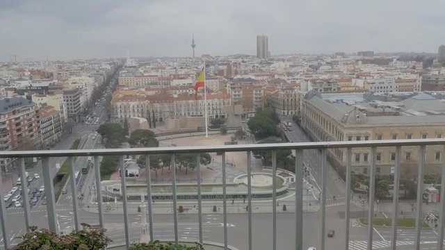 Panoramic of the square colon of madrid paseo de la castellana with flag of spain giant waving from height and behind a fence
