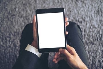 Mockup image of a business man sitting and holding black tablet pc with blank white screen with gray rug in background