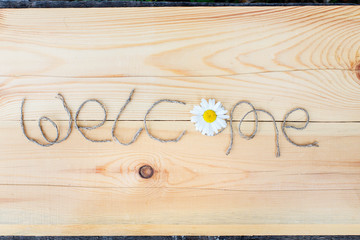 The inscription "Welcome" on a wooden background with wild flowers and copy space