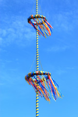 Teil eines Maibaums mit bunten Girlanden im Wind vor blauem Himmel