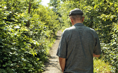 Mature man walks on a path in green forest in summer