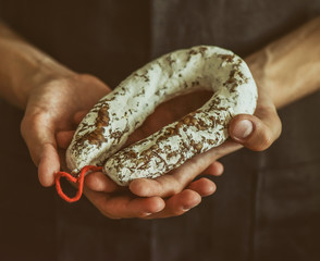 Hands are holding an artisan aged salami