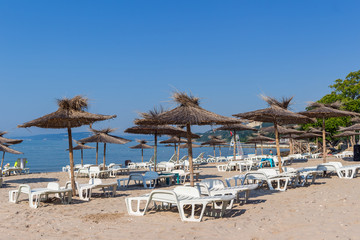 Black sea, sand beach with straw umbrellas and white sun chairs, Balchik, Bulgaria