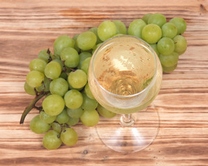 Glass of white wine and ripe organic green grapes isolated on vintage wooden background