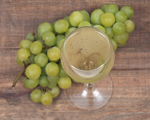 Glass of white wine and ripe organic green grapes isolated on vintage wooden background