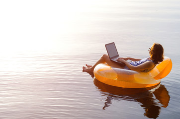 Business woman working on a laptop in an inflatable ring in the water, a copy of the free space....