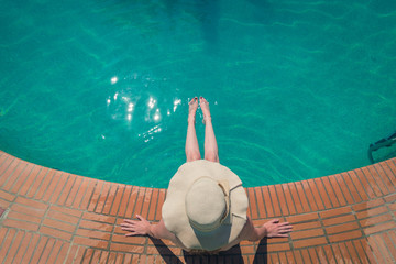 Beautiful woman in a hat sitting on the edge of the swimming pool