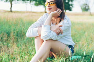 Beautiful young girl in a T-shirt jumping in the grass at sunset wearing yellow glasses, good mood, smiling