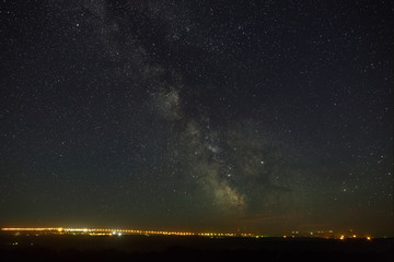 Starry night sky with the Milky Way over the city with lighting.