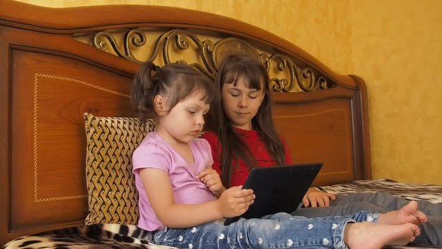 Children play on the tablet. Two little girls with a tablet.