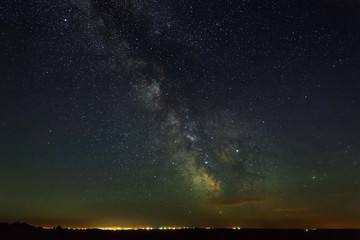 Starry night sky with the Milky Way over the city with lighting.