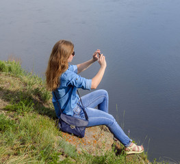 A young girl in blue clothes, wearing sunglasses, takes pictures in the summer on the street