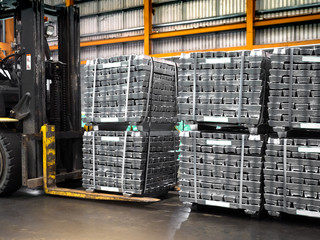 Stack of raw aluminum ingots in warehouse and handling by forklift.