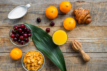 Light summer breakfast. Muesli, oranges, cherry and croissant on wooden table background top view