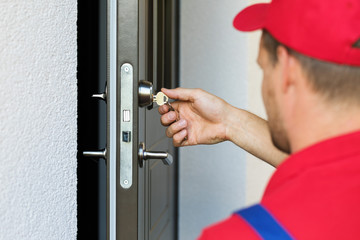 door lock service - locksmith working in red uniform - obrazy, fototapety, plakaty