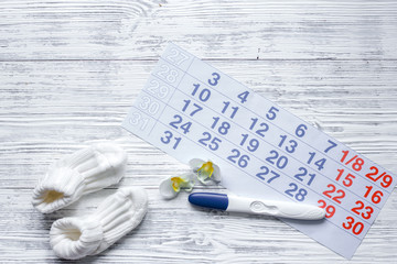 Pregnancy planning. Pregnancy test, calendar, pills and booties on wooden background top view copyspace