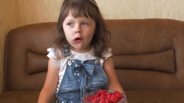 The girl eats raspberries. A little girl is eating raspberries.