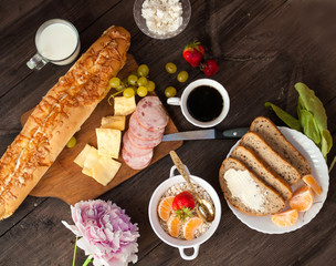 A varied breakfast, a sandwich with cheese, baguette and bread with butter and feta cheese with grapes and berries. Morning coffee and milk.