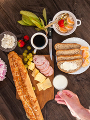 A varied breakfast, a sandwich with cheese, baguette and bread with butter and feta cheese with grapes and berries. Morning coffee and milk.
