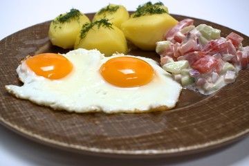 Fried egg and potatoes with salad on old brown plate.