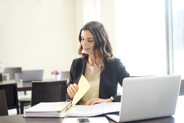 Doing some paperwork at office. Shot of a young professional woman sitting at desk in front of laptop and working on business conctract. 