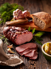  Sliced smoked ham  on a wooden  table with addition of fresh  herbs and aromatic spices.   Natural...