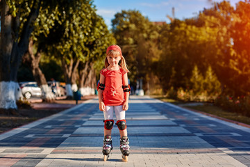Pretty little girl in red t-shirt learning to roller skate outdoors on beautiful summer day