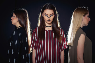Three unique models with an unusual make-up and in original clothes posing on a podium