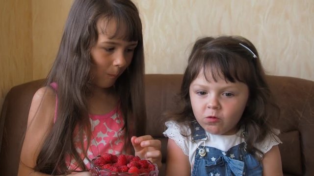 A child eats raspberries. Two sisters eat raspberries.