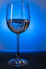 Stream of water flows into a transparent glass standing on a table on a blue background